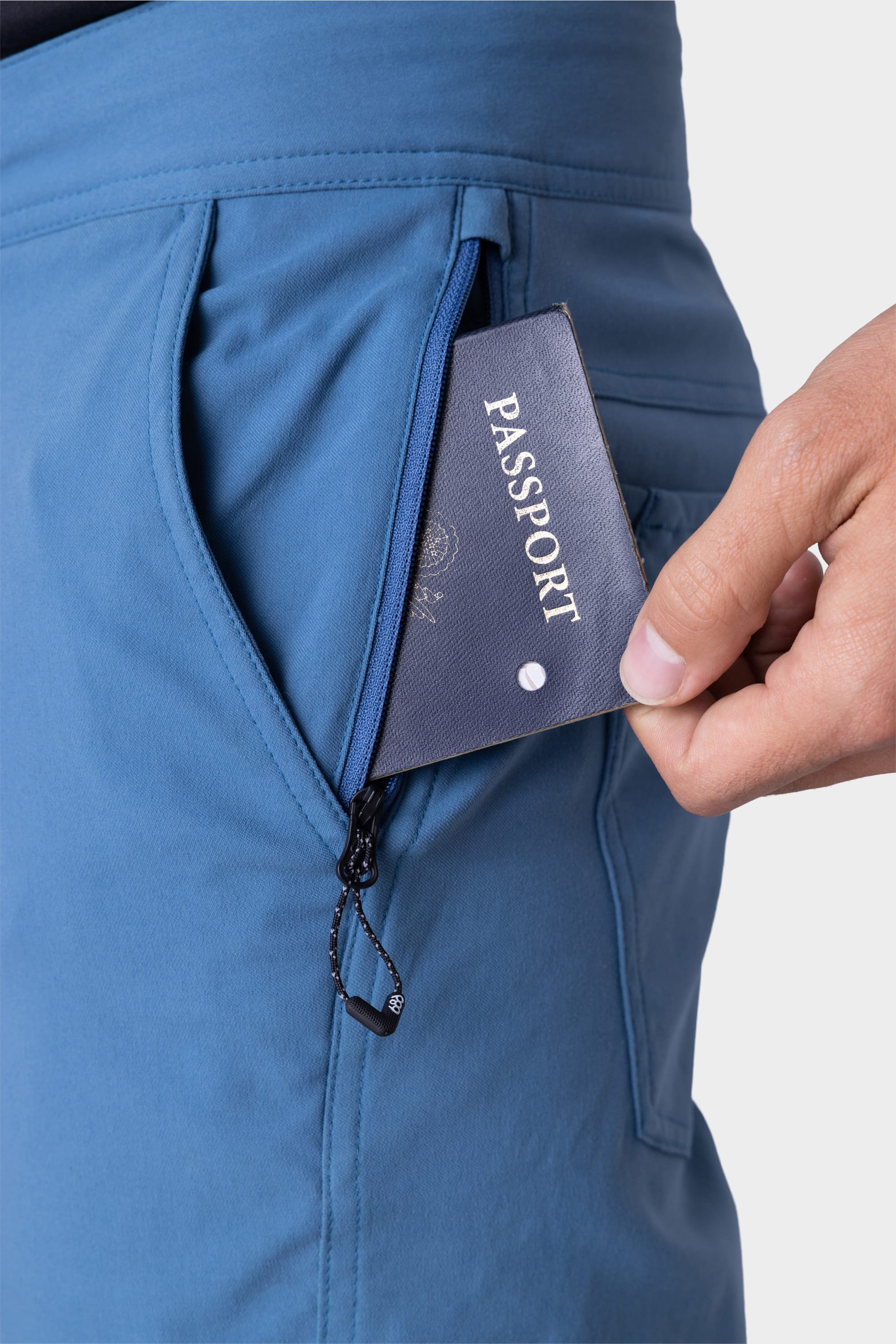 A hand places a passport into the zippered pocket of 686 Mens Platform Bike Pant - Slim Fit by 686, with focus on the pocket and passport against a plain background.