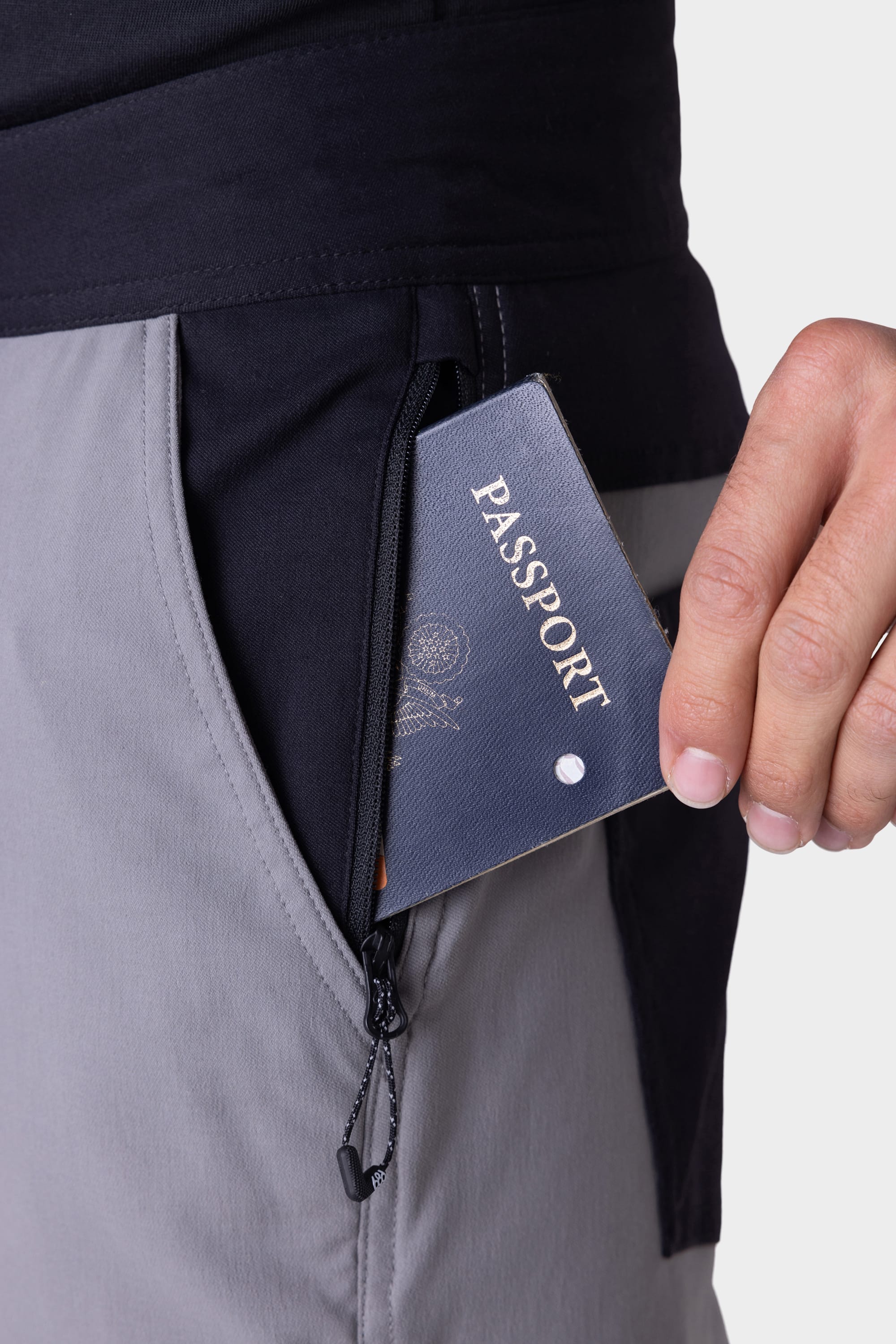 A hand places a passport into the zippered pocket of the 686 Mens Platform Bike Pant - Slim Fit, shown in grey and black against a plain white background.