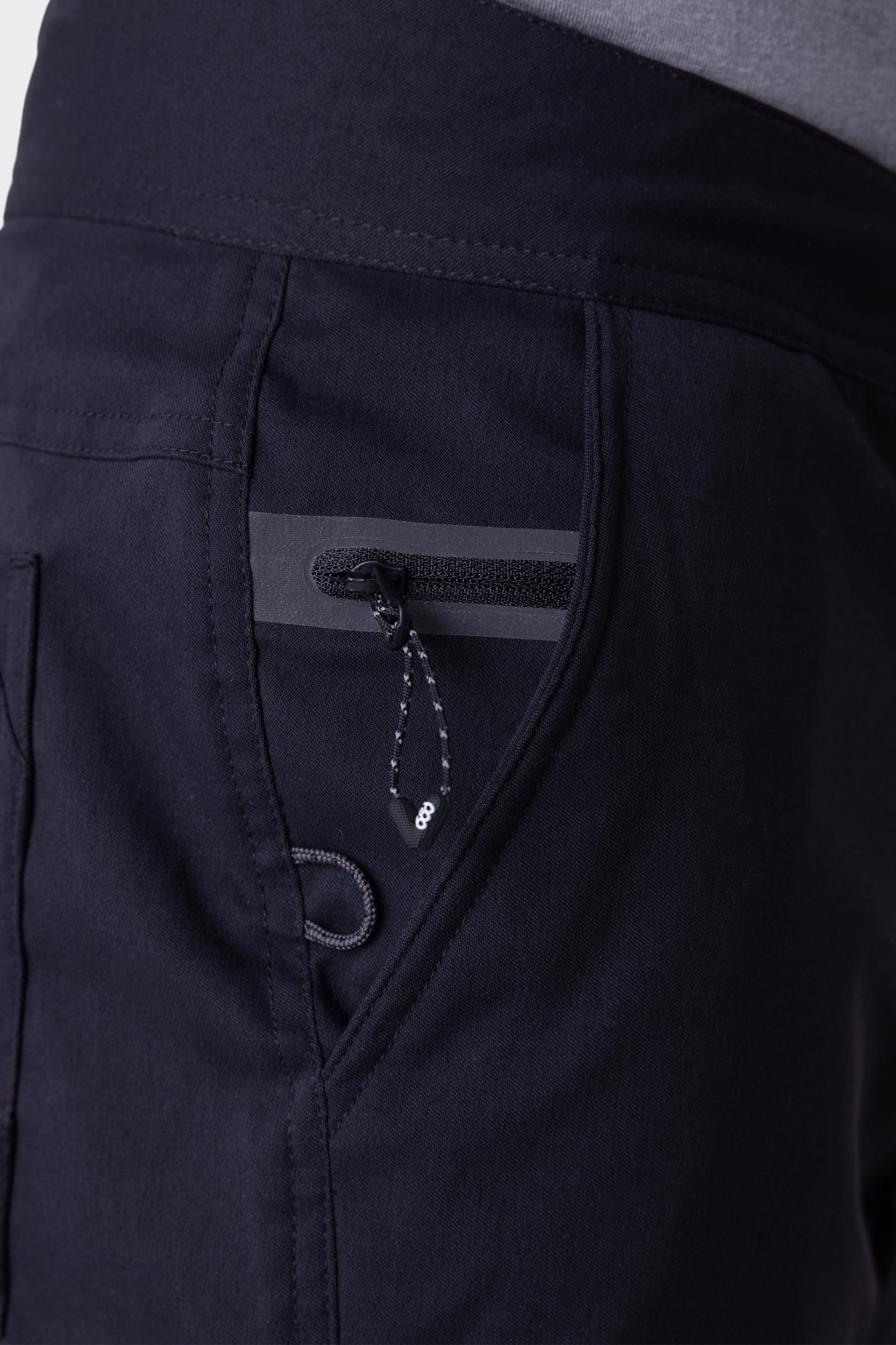 Close-up of the 686 Mens Platform Bike Pant - Relaxed Fit, featuring a zippered pocket with a cord pull, contrast stitching, and visible waistband with part of a tucked-in shirt.