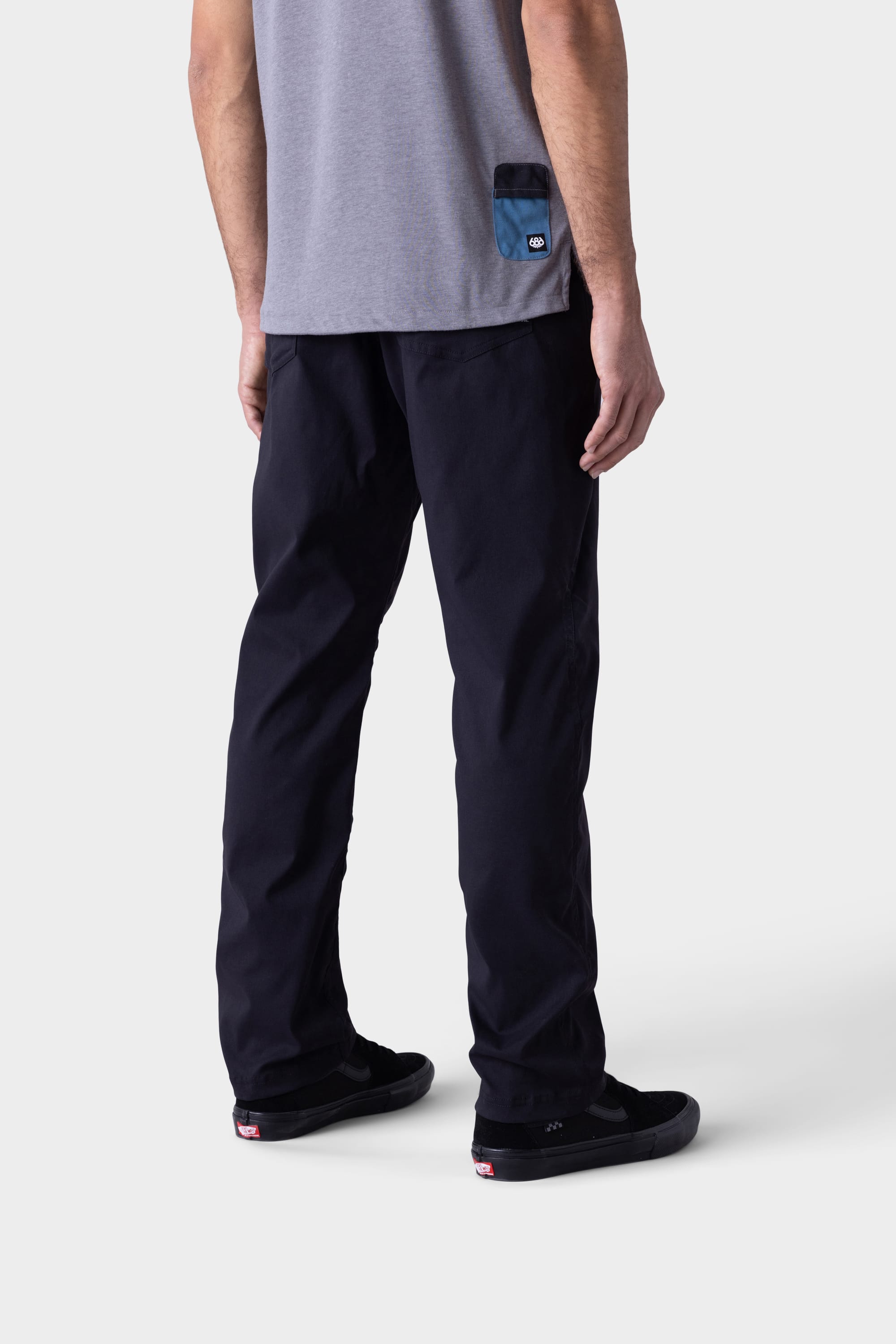 A person, visible from the waist down, wears black 686 Mens Platform Bike Pant - Relaxed Fit by 686 and black sneakers, standing against a plain light background.